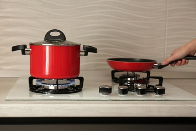 Photo of Woman putting frying pan near red pot on modern gas stove, closeup