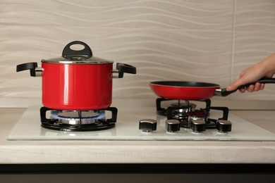 Woman putting frying pan near red pot on modern gas stove, closeup