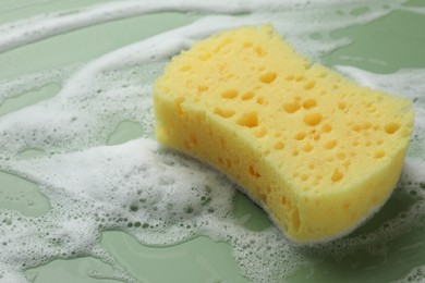 Photo of Yellow sponge with foam on green background, closeup