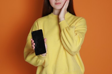 Woman showing damaged smartphone on orange background, closeup. Device repairing