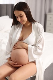 Photo of Beautiful pregnant woman in stylish comfortable underwear and robe on bed at home