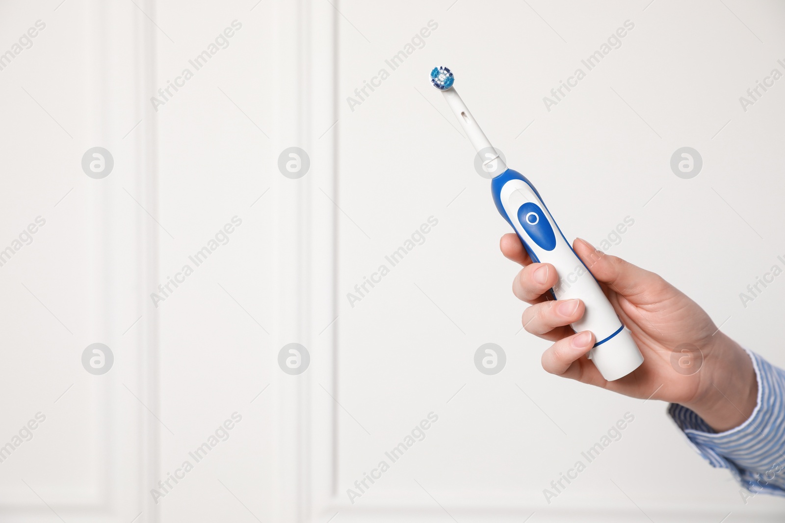 Photo of Woman holding electric toothbrush near white wall, closeup. Space for text