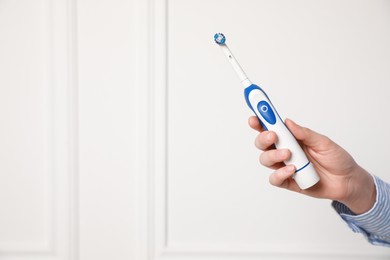 Woman holding electric toothbrush near white wall, closeup. Space for text