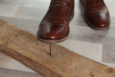 Photo of Careless man stepping on nail in wooden plank, closeup