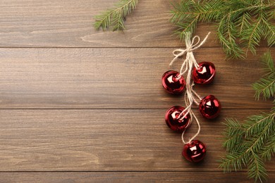 Photo of Shiny red sleigh bells and fir branches on wooden table, flat lay. Space for text