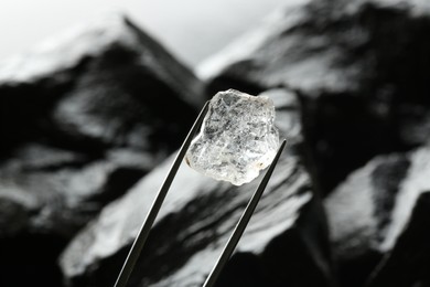 Photo of Tweezers with beautiful shiny diamond over stones, closeup