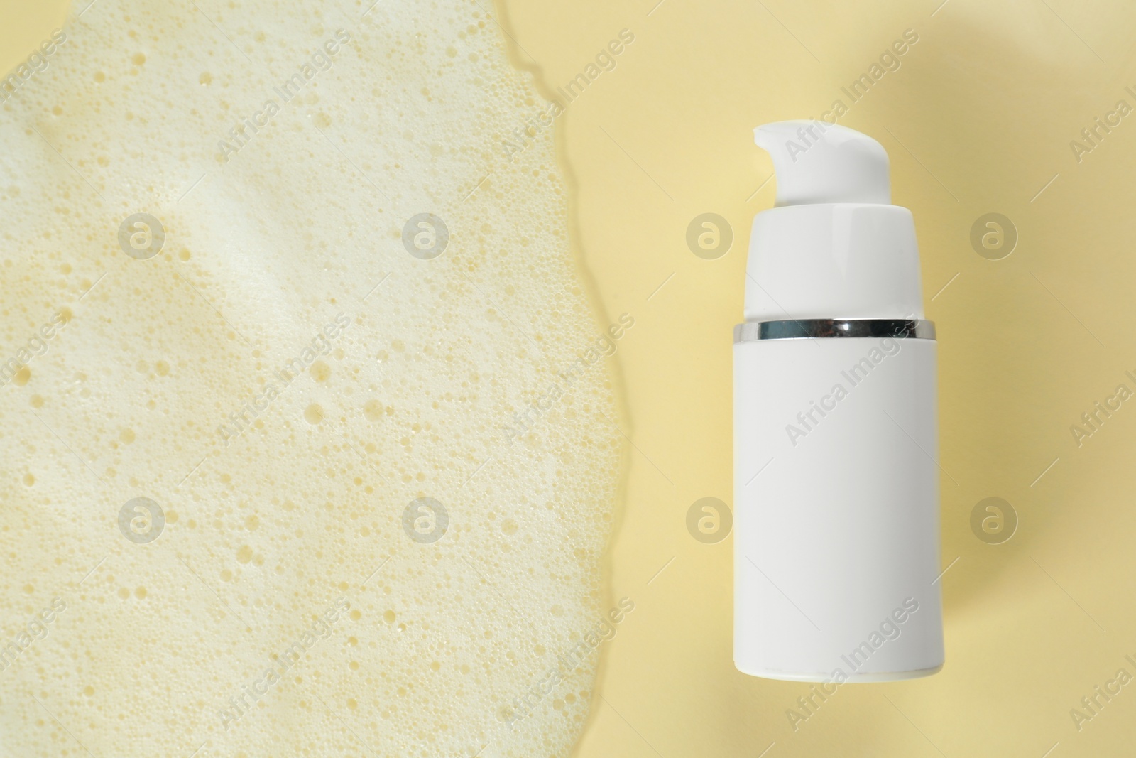 Photo of Bottle of face cleanser and white foam on beige background, top view with space for text. Skin care cosmetic