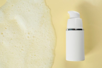 Photo of Bottle of face cleanser and white foam on beige background, top view with space for text. Skin care cosmetic