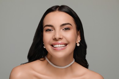 Young woman wearing elegant pearl jewelry on grey background
