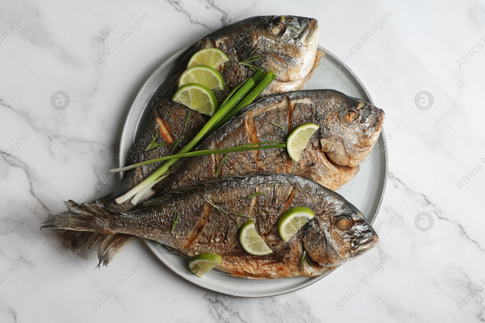 Photo of Delicious baked fish served with green onion and lime on white marble table, top view. Seafood