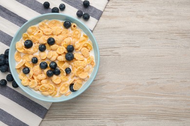 Photo of Bowl of tasty crispy corn flakes with milk and blueberries on wooden table, flat lay. Space for text