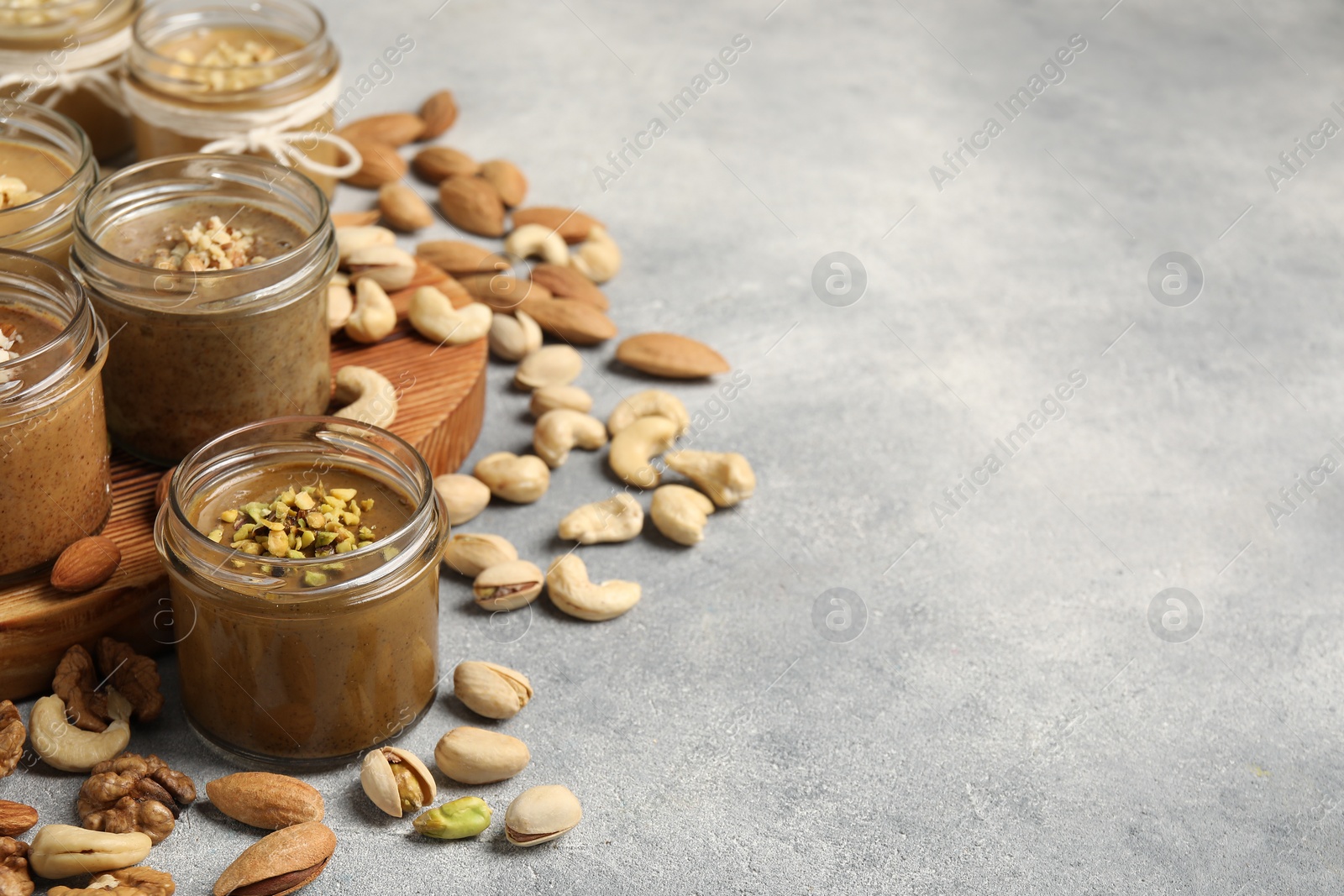 Photo of Tasty nut butters in jars and raw nuts on light grey table, space for text