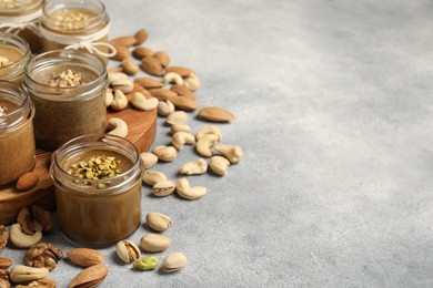 Tasty nut butters in jars and raw nuts on light grey table, space for text