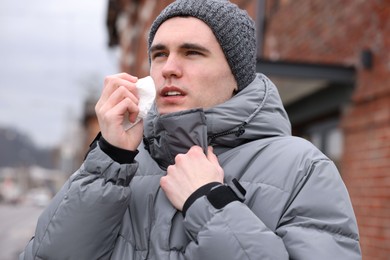 Photo of Sick young man with tissue on city street. Cold symptoms