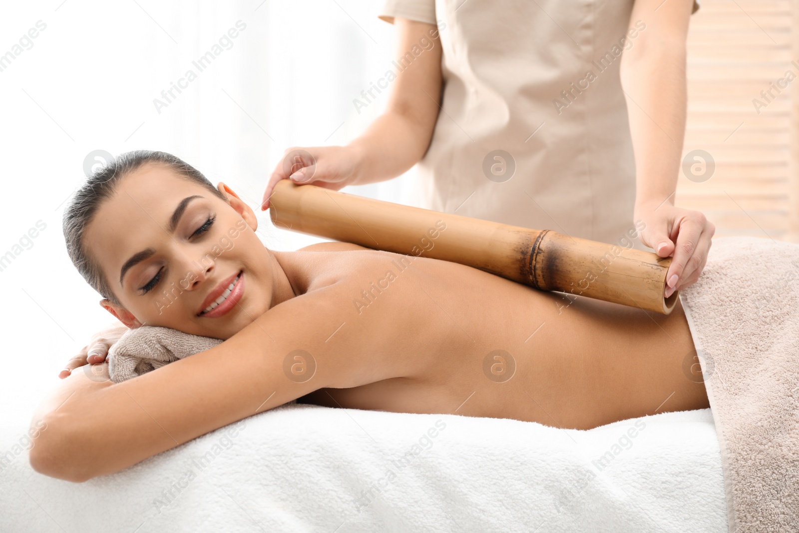 Photo of Young woman having massage with bamboo stick in wellness center