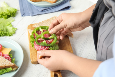 Woman making sandwich with green bell pepper and sausage at white table, closeup