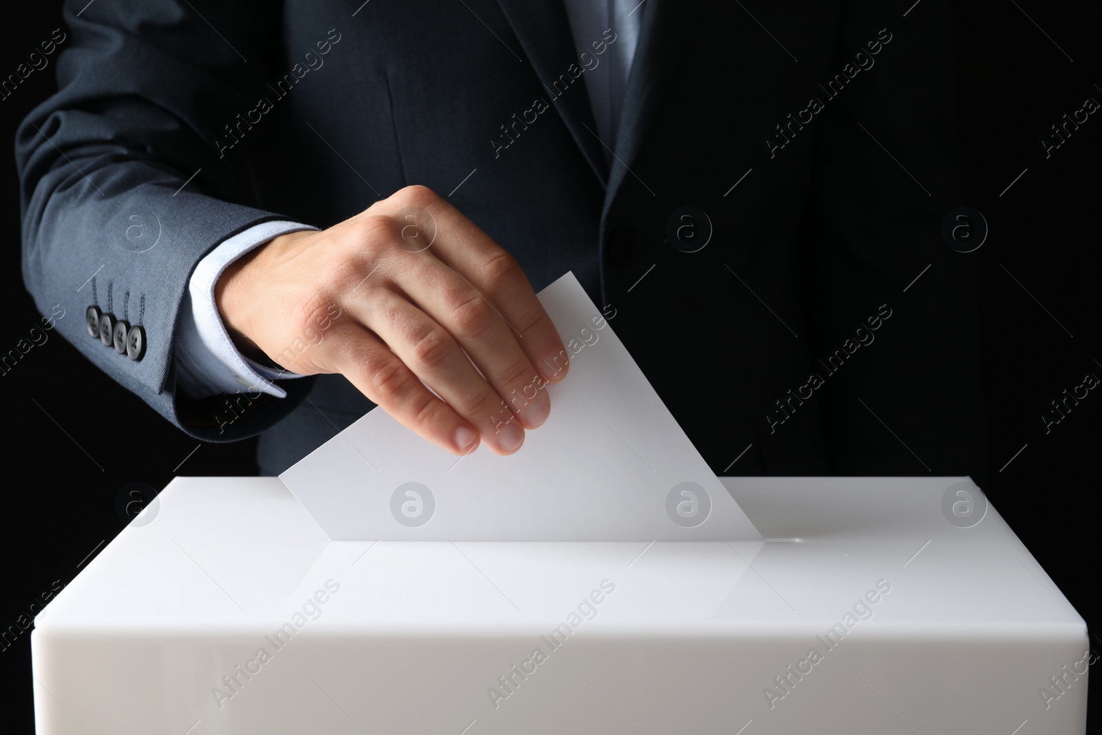 Photo of Man putting his vote into ballot box on black background, closeup