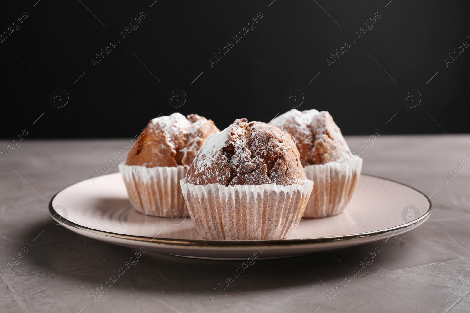 Photo of Tasty muffins with sugar powder on grey textured table, closeup