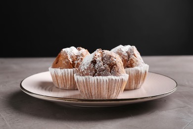 Photo of Tasty muffins with sugar powder on grey textured table, closeup