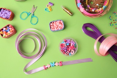 Photo of Handmade jewelry kit for children. Colorful beads, ribbons and supplies on green background, flat lay