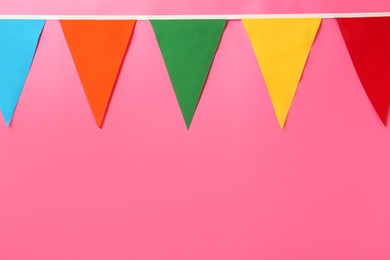 Photo of Bunting with colorful triangular flags on pink background. Space for text