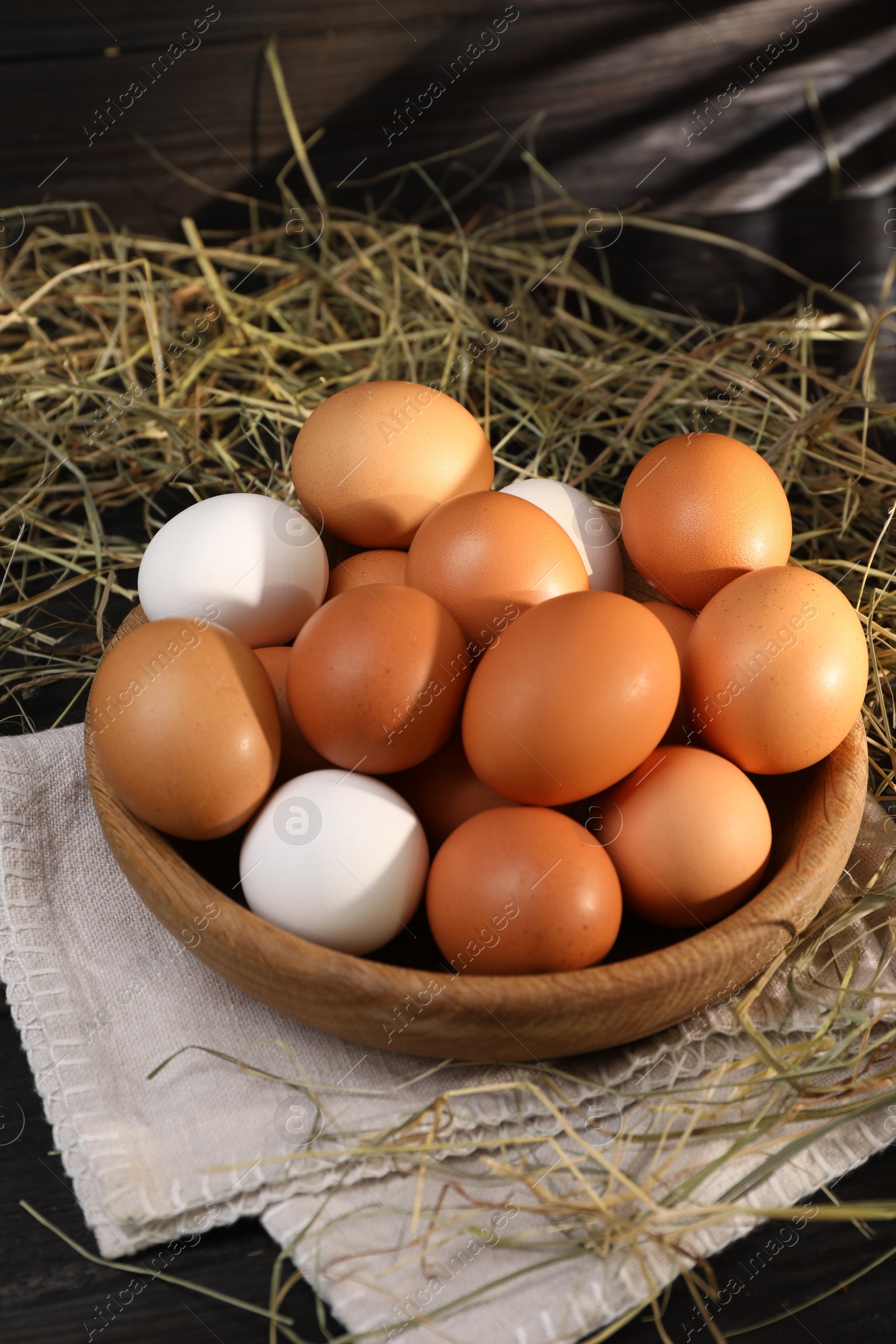Photo of Fresh chicken eggs in bowl and dried hay on black wooden table