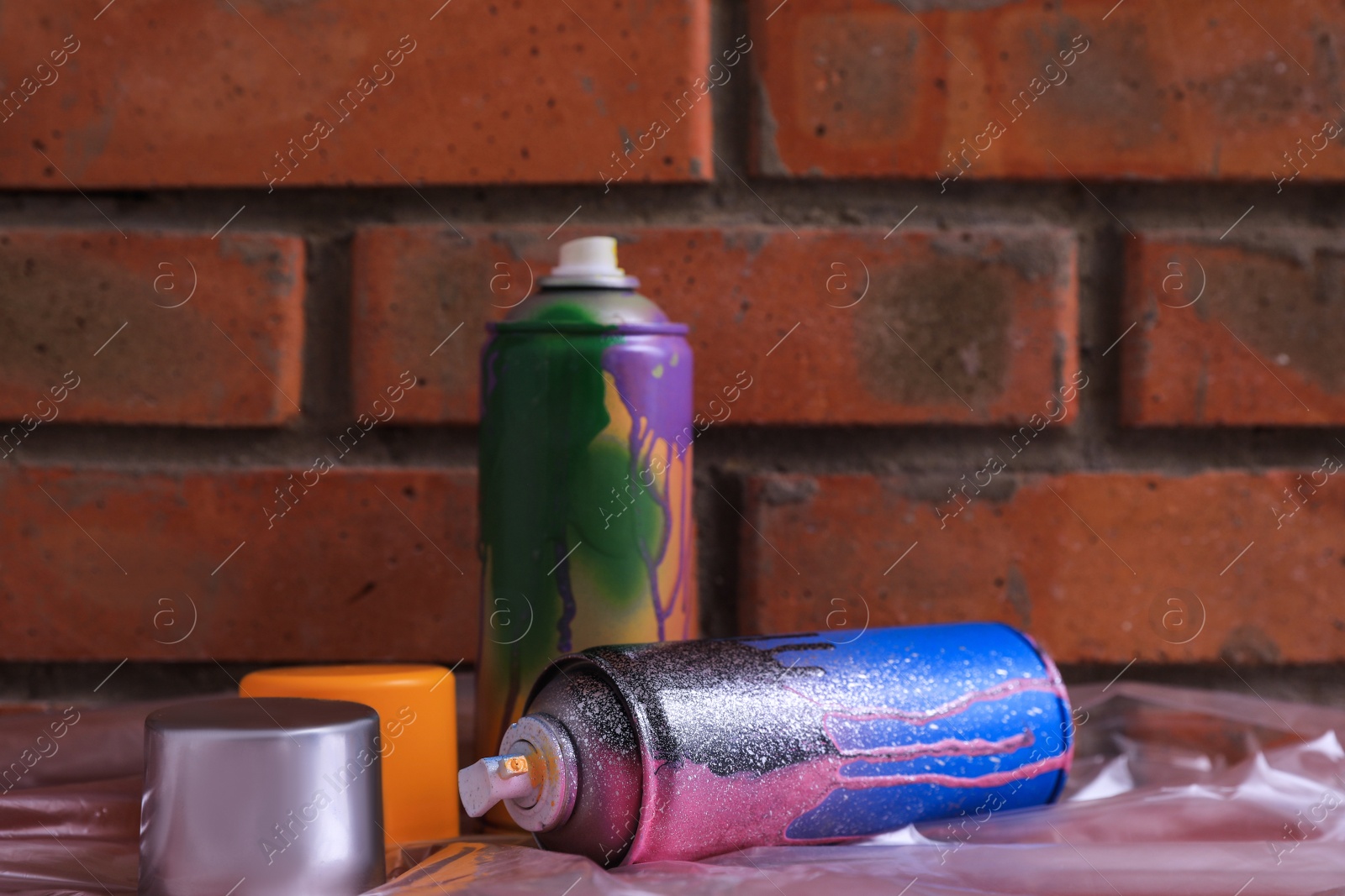 Photo of Used cans of spray paints on table near brick wall. Graffiti supplies