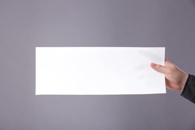 Photo of Man holding sheet of paper on grey background, closeup. Mockup for design