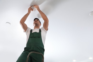 Photo of Electrician in uniform repairing lamp on ceiling indoors. Space for text