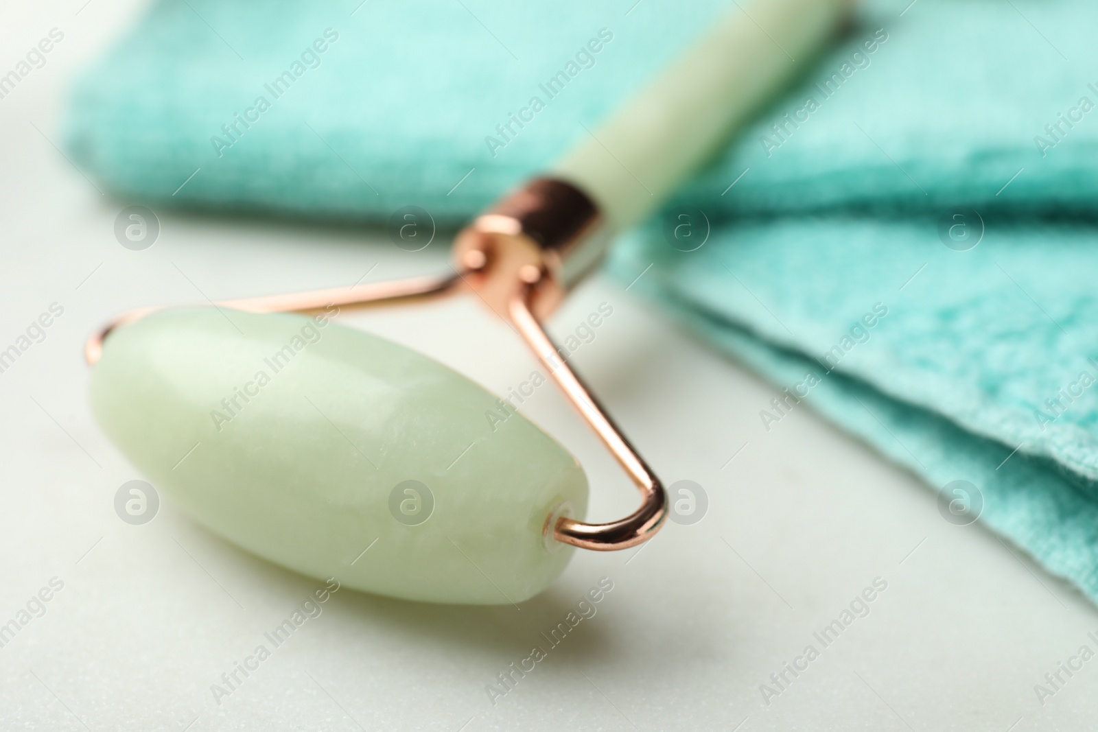 Photo of Natural jade face roller and towel on light background, closeup