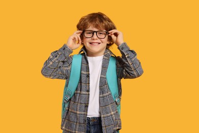 Happy schoolboy with backpack on orange background