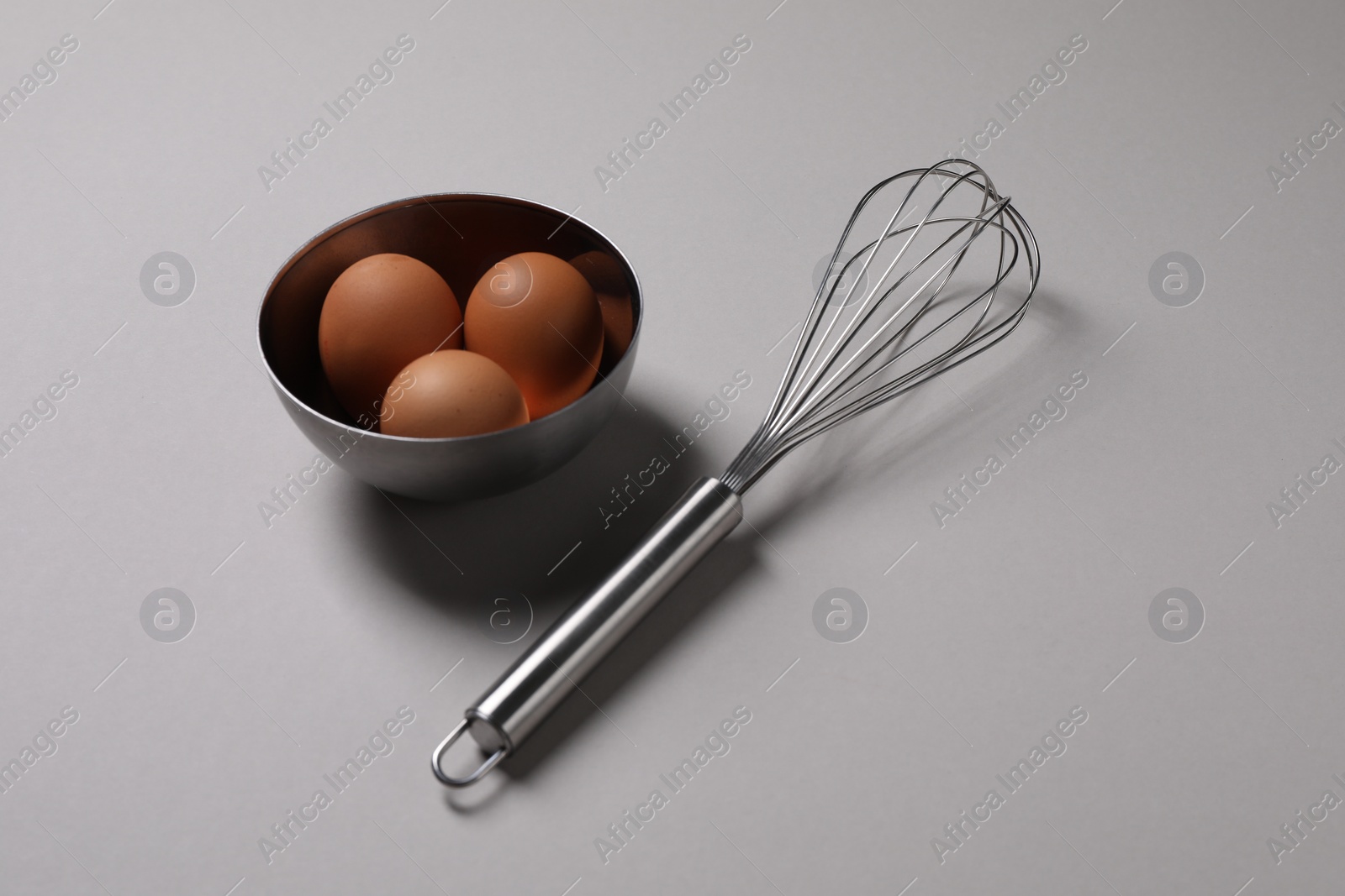 Photo of Metal whisk and raw eggs on grey background