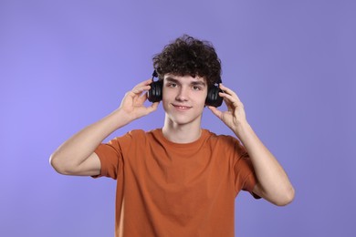 Cute teenage boy listening music with headphones on violet background