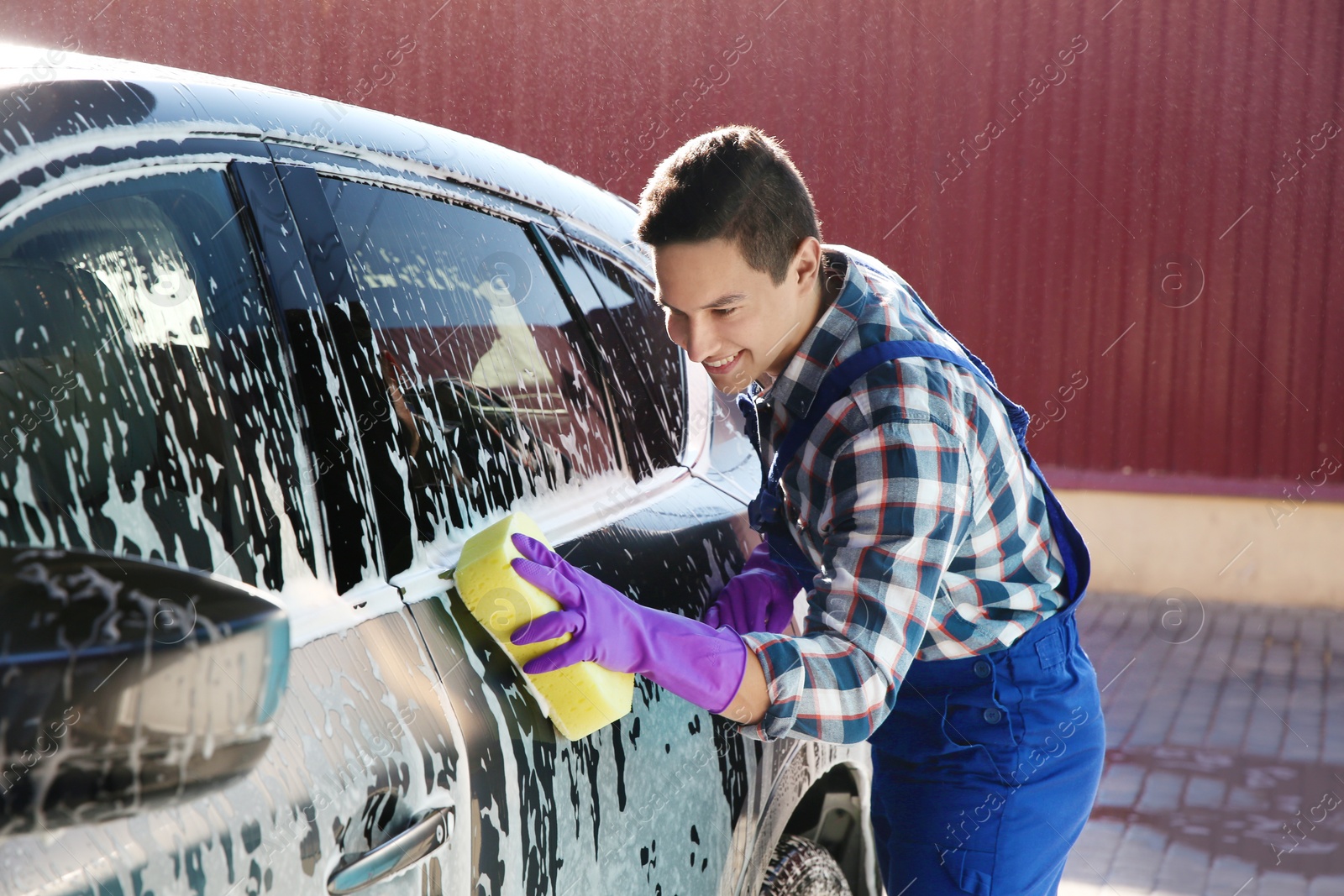 Photo of Worker cleaning automobile with sponge at car wash