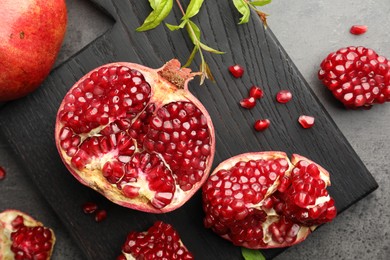 Photo of Cut fresh pomegranate and green leaves on grey table, top view