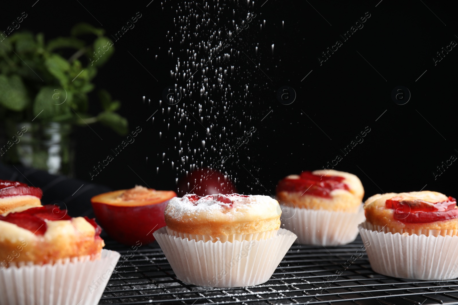 Photo of Sprinkling plum cupcakes with powdered sugar at table