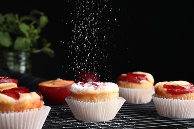 Photo of Sprinkling plum cupcakes with powdered sugar at table