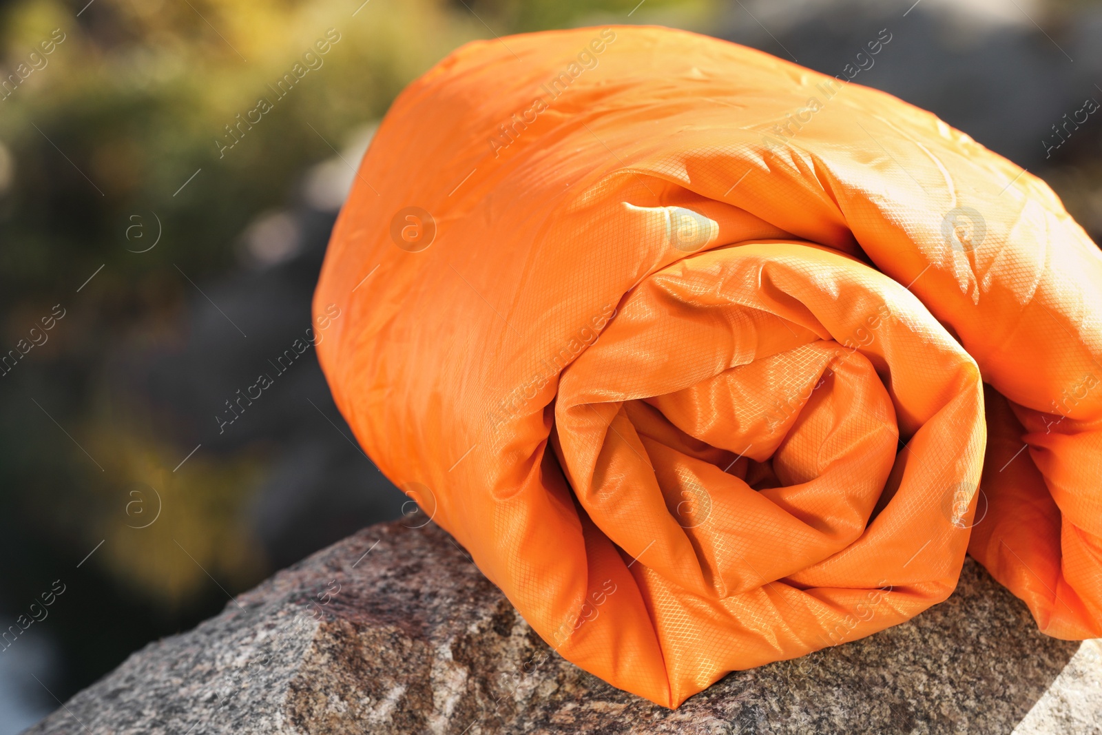 Photo of Orange sleeping bag on rock outdoors. Camping equipment