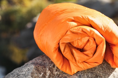 Photo of Orange sleeping bag on rock outdoors. Camping equipment