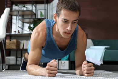 Photo of Handsome man doing plank exercise on floor at home