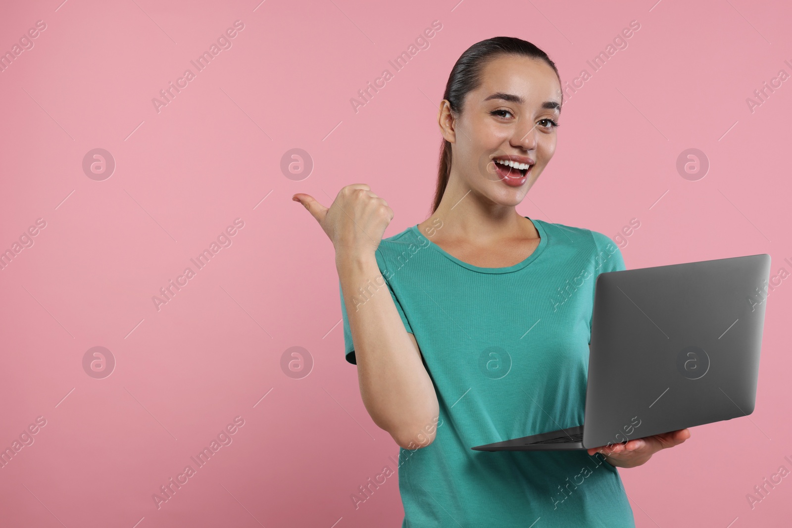 Photo of Special promotion. Smiling woman with laptop pointing at something on pink background. Space for text