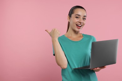 Photo of Special promotion. Smiling woman with laptop pointing at something on pink background. Space for text