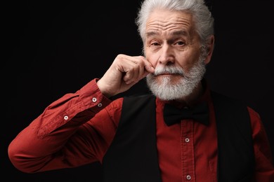 Senior man touching mustache on black background