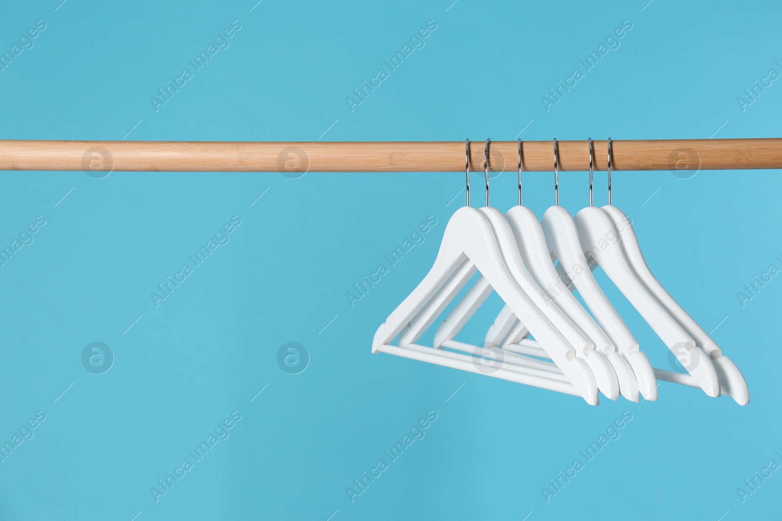 Photo of Wooden rack with clothes hangers on color background, space for text