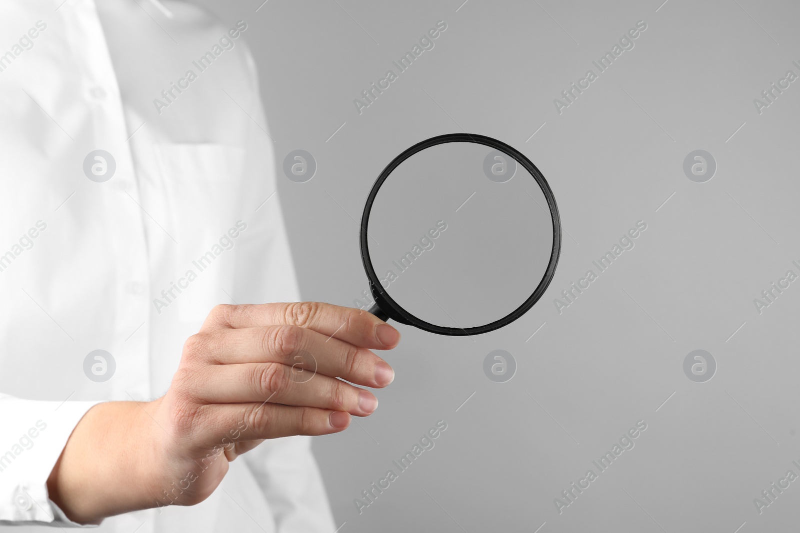 Photo of Woman holding magnifying glass on grey background, closeup. Find keywords concept