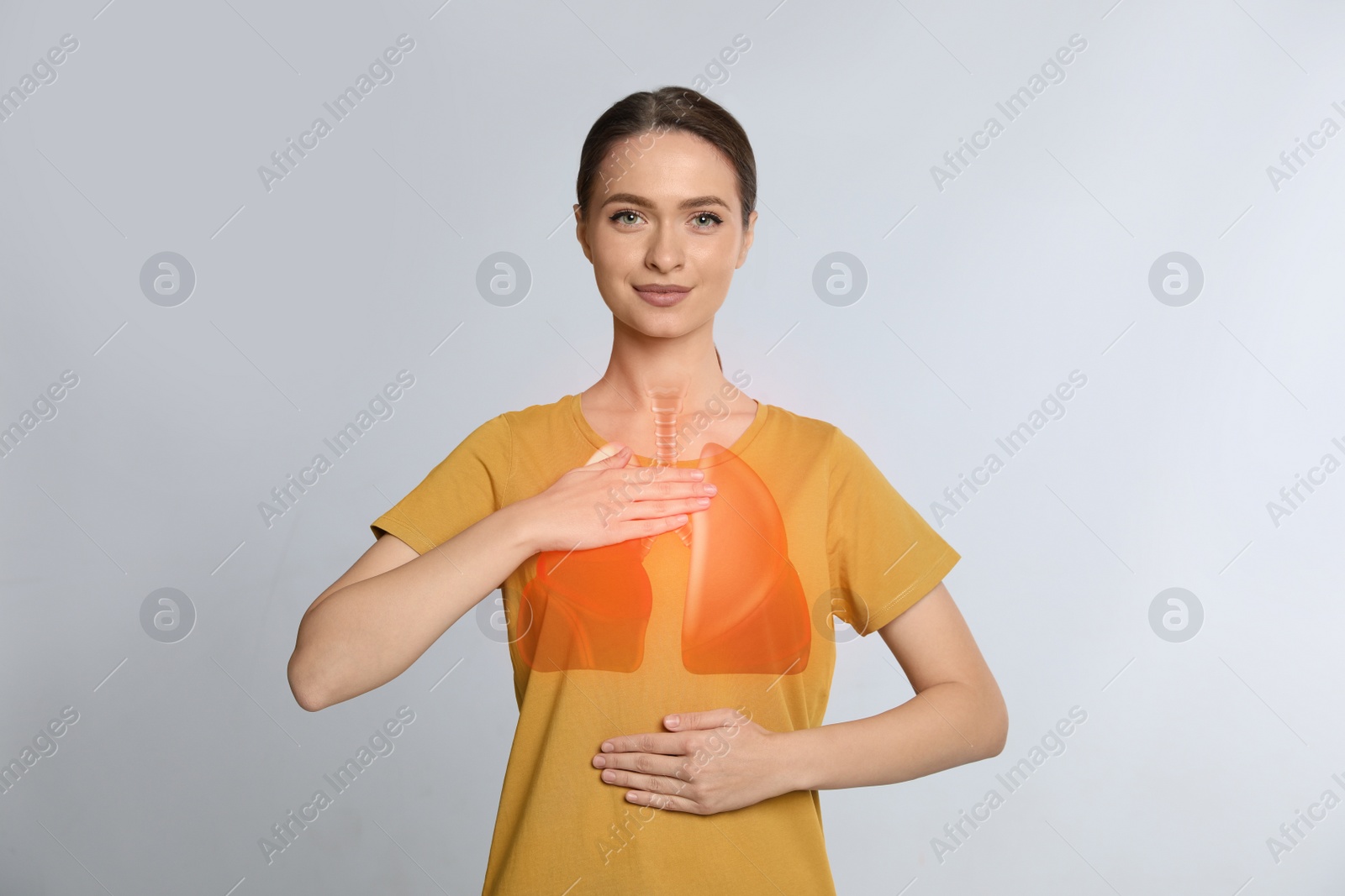 Image of Young woman holding hands near chest with illustration of lungs on light grey background