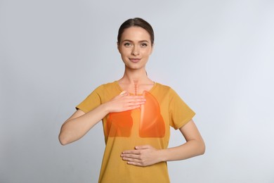 Young woman holding hands near chest with illustration of lungs on light grey background