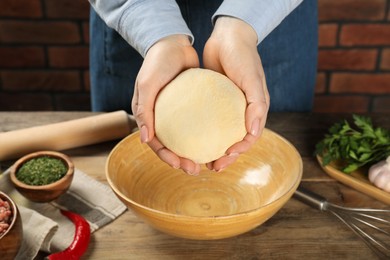 Photo of Woman holding raw dough at wooden table, closeup