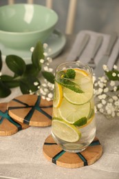 Glass of lemonade and stylish wooden cup coasters on light table