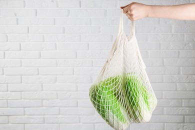 Photo of Woman holding string bag with fresh Chinese cabbages near white brick wall, closeup. Space for text